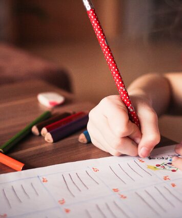 A girl drawing on paper on the floor, showcasing creativity and artistic expression.