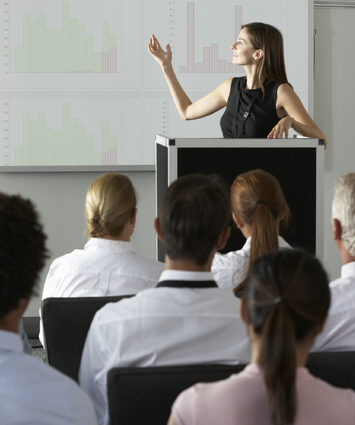 Businesswoman delivering presentation at conference, showcasing expertise and engaging audience in professional setting.