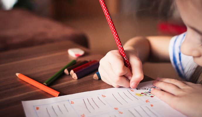 A girl drawing on paper on the floor, showcasing creativity and artistic expression.